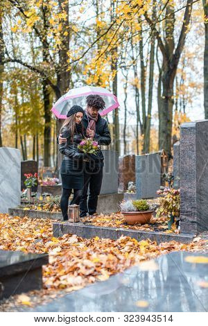 Couple mourning a deceased loved one on cemetery in fall standing between the graves