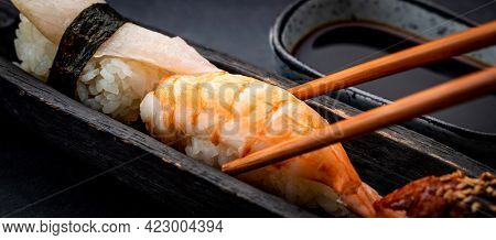 Closeup view on sushi sashimi set with shrimps and soy sauce served with wooden chopsticks on black taable. Traditional japanese meal composition with rice and seafood