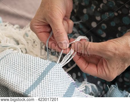 Elderly Woman Is Creating A Fringe On A Woven Shawl. Hands Of Artisan At Work