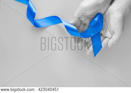 Hands Holding Deep Blue Ribbon On Blue Background With Copy Space. Colorectal Cancer Awareness Colon
