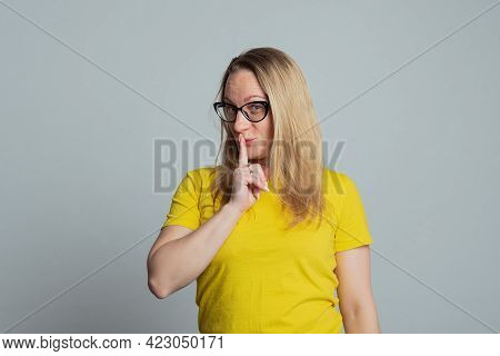 Portrait Of Mature Woman In Glasses Keeping Finger At Her Mouth, Saying Shh, Hush, Tsss, Wearing Cas