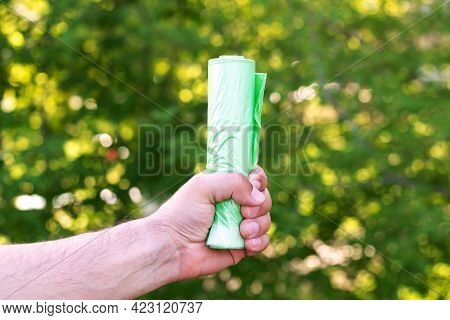 Man Holding Eco Plastic Green Garbage Bio Bag In Roll Outdoors