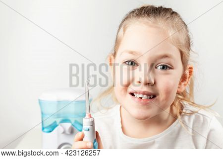 Water Flosser. Cute Little Girl With An Irrigator On A White Background. Oral Hygiene, Prevention Of