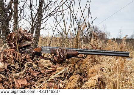 A Camouflaged Duck Hunter Sits In A Masked Duck Blind. He Aims His Shotgun At The Target. There Are 