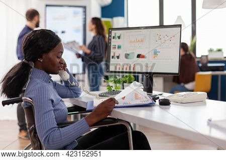 Busy Paralysed Handicapped Black Employee Answering Phone Talking With Colleague Sitting Immobilized