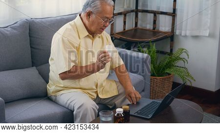 Asian Elderly Patient Video Call By Laptop Computer To Doctor For Inquire About Which Bottle Of Medi