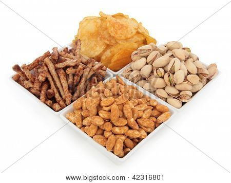 Potato crisps, pistachio nuts, roasted peanuts and twiglet savoury snacks in porcelain dishes over white background. Selective focus.