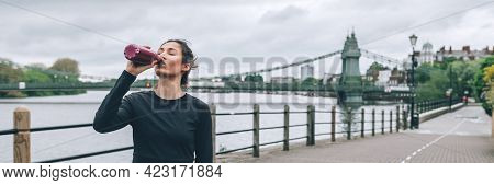 Beautiful Young Slim Woman Is Drinking Water While Jogging Along The Embankment Of The River In Lond