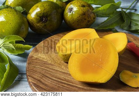 Selective Focus On Ripe Mango Slices On Wooden Chopping Board Along With Mangoes And Leaves On Woode