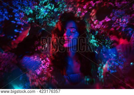A Fantastic Shot Of A Girl In Flowers With Neon Multicolored Light And Phantasmagoria. The Concept O