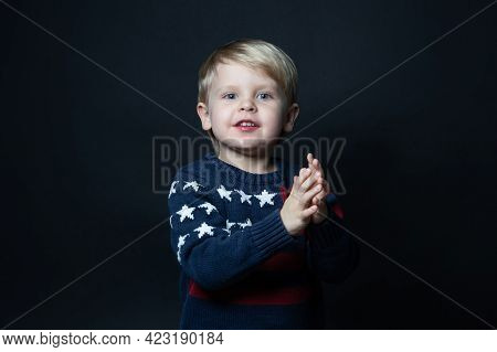 Boy In Sweater With Usa American Flag Claps His Hands On Black Background With Copy Space.
