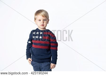 Cute Boy In A Sweater With An American Flag Is Showing Something On A White Background With A Copy S
