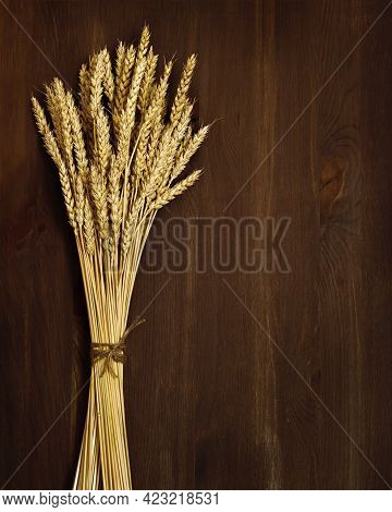 Bunch Of Compressed Stems With Ears. Golden Wheat On Dark Brown Wooden Background. Wheat Close Up. R