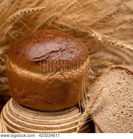 Whole Loaf Of Crispy Wheat Bread. Slice Of Bread And Wheat Spikelets On Blurred Background. Healthy 
