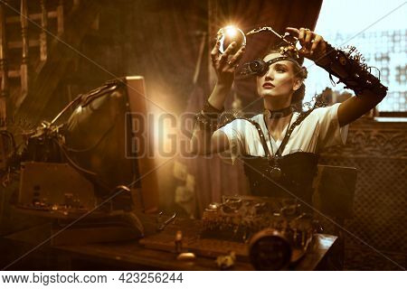 World of steampunk. Beautiful steampunk lady scientist inventor works in her laboratory with Victorian interior. 