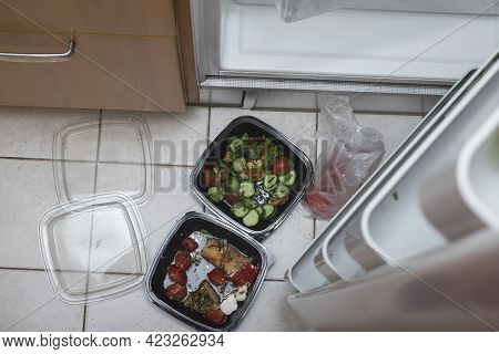 Food In Plastic Containers Seemingly Gone Off On A Floor Next To Open Fridge