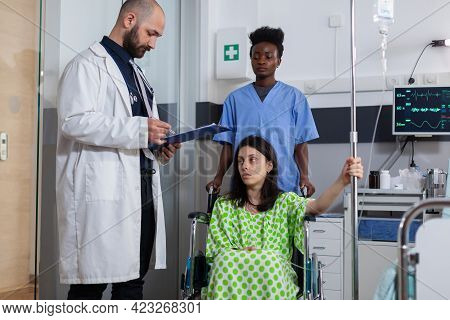 Man Doctor Writing Healthcare Expertise On Clipboard Working Hospital Ward. Black Asisstant Woman Pu