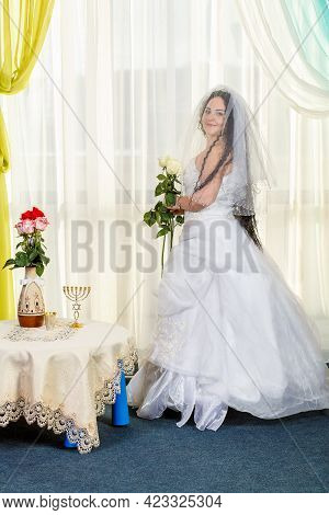 A Joyful Jewish Bride With Her Face Covered With A Veil And A Bouquet Of White Roses Is Standing In 
