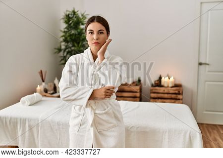 Young beautiful hispanic woman wearing bathrobe at wellness spa thinking looking tired and bored with depression problems with crossed arms. 