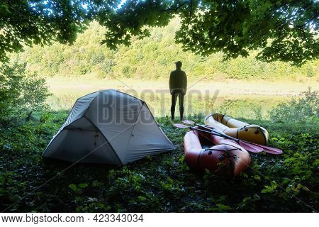Man near tent and packrafts in forest camp near river. Packrafting. Active lifestile concept