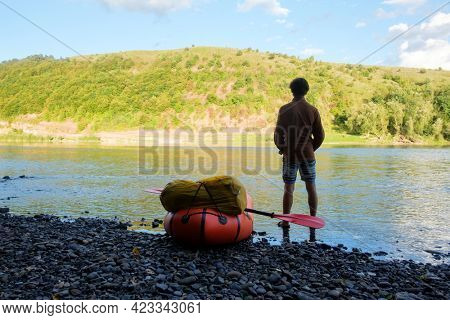 Tourist near yellow packraft rubber boat ready for adventures with red padle on a sunrise river. Packrafting. Active lifestile concept