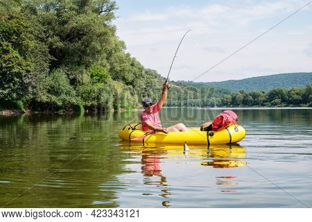 Mature man fishing from the packraft yellow boat on the river at summer time