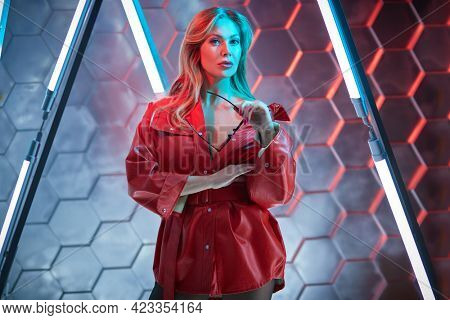 Modern middle-aged woman in red leather jacket posing in the light of neon lamps. Techno style, disco. Fashion shot.