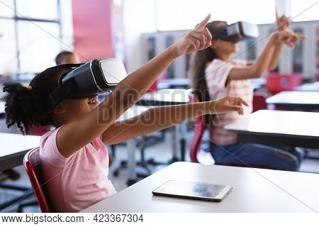 African american girl wearing vr headset gesturing while sitting on her desk in the class at school. school and education concept