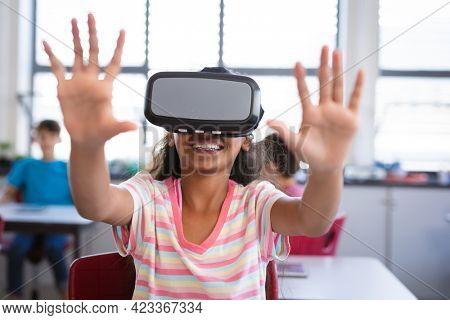 African american girl wearing vr headset gesturing while sitting on her desk in the class at school. school and education concept
