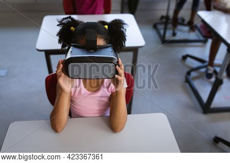 African american girl wearing vr headset while sitting on her desk in class at school. school and education concept