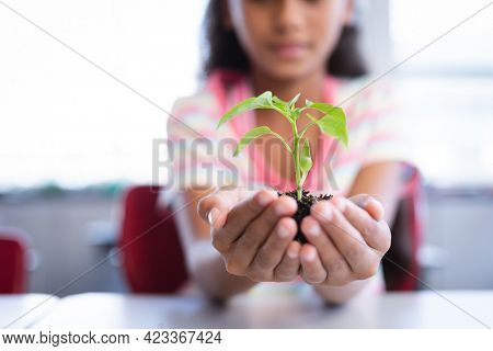 Mid section of girl holding a plant seedling while sitting on her desk in class at school. school and education concept