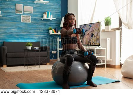 African Woman Using Stability Ball Keeping Outstretched Arms Working Out Shoulders Using Blue Dumbbe