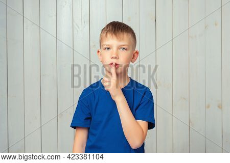 Portrait Of Cute Preteen Boy In Blue T Shirt Keeping Finger At Her Mouth, Saying Shh, Hush, Tsss. Si