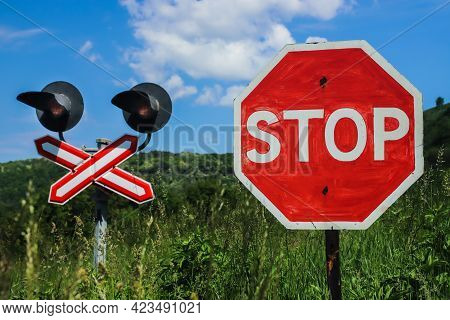 Stop Sign In Front Of A Railway Crossing On A Background Of Blue Sky With Clouds