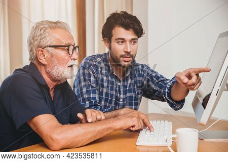 Young Man Or Son Teaching His Grandfather Elderly Dad Learning To Using Computer At Home.