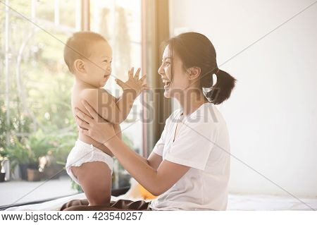 Asian Mom Smiling Happy Holding And Playing With Her Son In Living Room. Mom And Baby Clap Your Hand