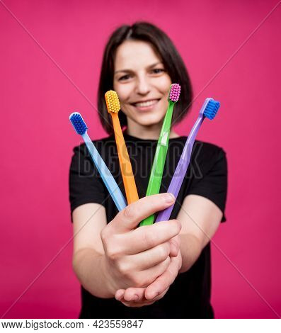 Beautiful Happy Young Woman With Different Colored Toothbrushes On Blank Pink Background