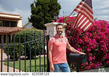 Smiling Real Estate Agent Near New Residence To Sale, Outside. Rent New Home With Amarican Flag.