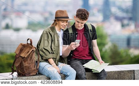 Young Couple Travelers With Map In City On Holiday, Using Smartphone.