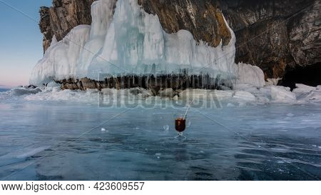 The Base Of The Granite Rock Is Covered With Icicles. There Is A Glass Mug With Mulled Wine On The I
