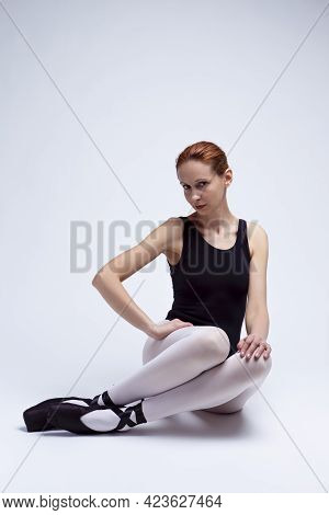 Professional Female Ballet Dancer In Body Suit Posing With Legs Folded White On Floor.