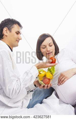 Portrait Of Man Offering His Pregnant Wife Fresh Vegetables On Glass Bowl Over White Background.