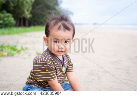 Cute Child Little Boy 1 Year Old Sitting On Sand Beach At Coast. He Was Playing With Fun In Holidays