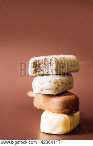 Different Chocolate Popsicles Lying On Top Of Each Other. Brown Background. Top Popsicle Bitten