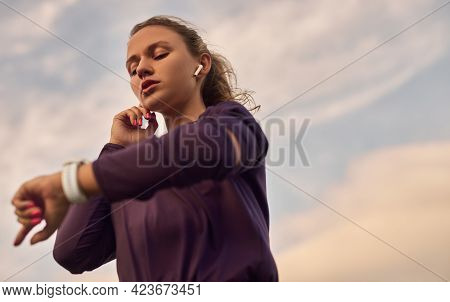 Low Angle Of Active Young Woman In Sportswear With Tws Earbuds Checking Notifications On Smartwatch 