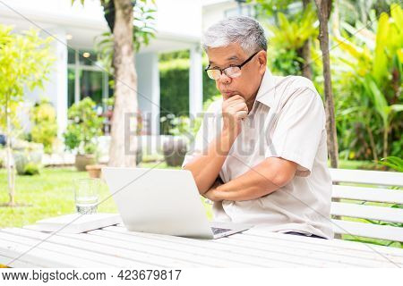 Portrait Of Old Elderly Asian Man Using A Computer Laptop In The Backyard For Learning New Skill Aft