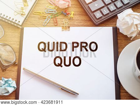 On A Wooden Table There Is An Office Sheet Of Paper With The Text Quid Pro Quo. Business Workspace W
