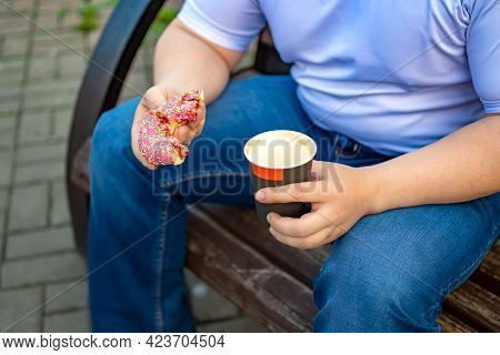 Closeup, A View Of A Bun, A Sweet Doughnut And A Half-drunk Cup Of Coffee, Tea In The Hand Of A Man 