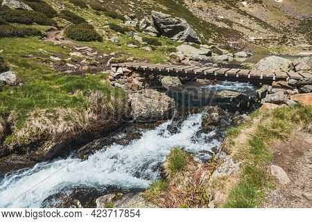 Wooden Bridge Over A River In The Middle Of The Mountain.