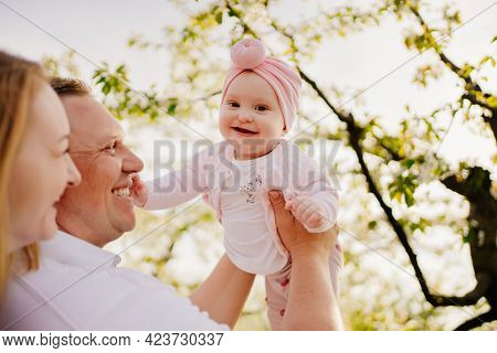 Mom, Dad And Daughter In Spring Flowering Garden. Cleft Lip In Infants.